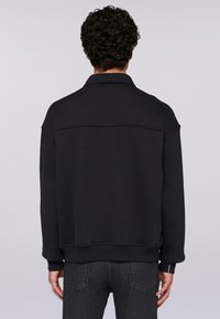 Svart sweatshirt med krage, nedsänkta axlar och ribbade manschetter. Slät yta med en subtil söm tvärs över den övre ryggen.