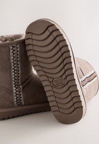 Stivali invernali marroni con rifinitura decorativa cucita e fodera in pelliccia, con suola testurizzata che mostra la misura "NEXT UK 12".