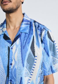 Short-sleeve shirt featuring a blue abstract pattern with varying textures and shapes, button-down front, and a relaxed collar design.