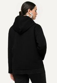 Hoodie noir avec une grande capuche à l'arrière, poche kangourou et poignets côtelés. Texture de tissu douce avec une coupe décontractée et relaxée.