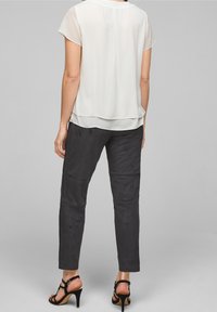 Blusa bianca a maniche corte con design a strati abbinata a pantaloni neri aderenti con una texture liscia e cuciture laterali. Sandali neri con tacco alto.