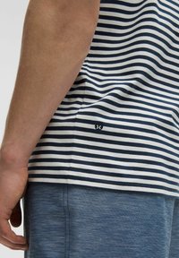 Chemise rayée bleu marine et blanche avec une coupe décontractée. Présente un petit logo sur l'ourlet. Le tissu semble doux avec une texture lisse.