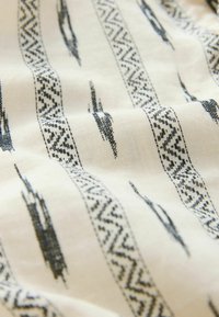 Tissu en coton avec un fond crème et des motifs géométriques noirs et des lignes ondulées. Le design inclut des zigzags et des rayures.