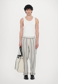 White tank top, striped wide-leg pants in beige and gray, black leather shoes, holding a two-tone bag with a structured design.