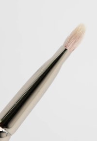 Makeupbørste med en avsmalnende, syntetisk bustetipp i lys rosa, festet til et skinnende, metallisk sølvhåndtak med glatt overflate.