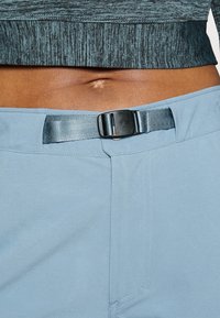 Ljusblå träningsbyxor med en strukturerad svart midja, försedda med ett bälte med en svart spänne och en mjuk tygfinish.