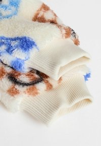 Weicher Fleece-Stoff mit blauen, braunen und schwarzen abstrakten Mustern, ausgestattet mit cremefarbenen, ribbeligen Strickbündchen.