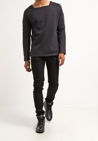 Top negro de manga larga con un corte amplio, que presenta un escote ancho. Combinado con jeans negros ajustados y botas negras con cordones.