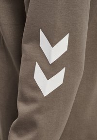 Bruine sweatshirt met een gestructureerde stof en twee witte chevronontwerpen op de linkermouw.