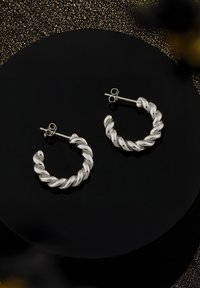 Silver snurrade hoopörhängen med en polerad yta och bakstängning, visade på en svart rund yta.