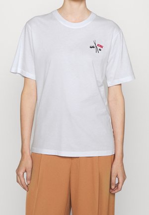 Biała bawełniana koszulka z krótkim rękawem, z małym czarno-czerwonym wzorem graficznym na piersi i luźnym krojem.