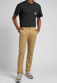 Svart bomullst-shirt med ficka, beige chinos med bälteöglor, och grå sneakers med vita accenter, uppvisade i en stående position.