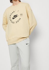 Ljusgul Nike-tröja med svart logotyp och texttryck, kombinerad med ljusgrå sweatpants som också visar en liten svart logotyp.