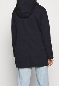 Giacca parka navy con cappuccio, realizzata in tessuto leggero, con taglio dritto, cuciture in vista e design di lunghezza media.
