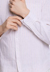 Camisa de botonera con rayas verticales en rosa claro y azul marino, hecha de una tela suave. Presenta botones y puños blancos, con un bolsillo en el pecho.