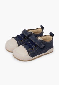 Modré plátěné boty s bílými gumovými špičkami a podrážkami. Mají suchý zip, kontrastní prošívání a texturovaný povrch.