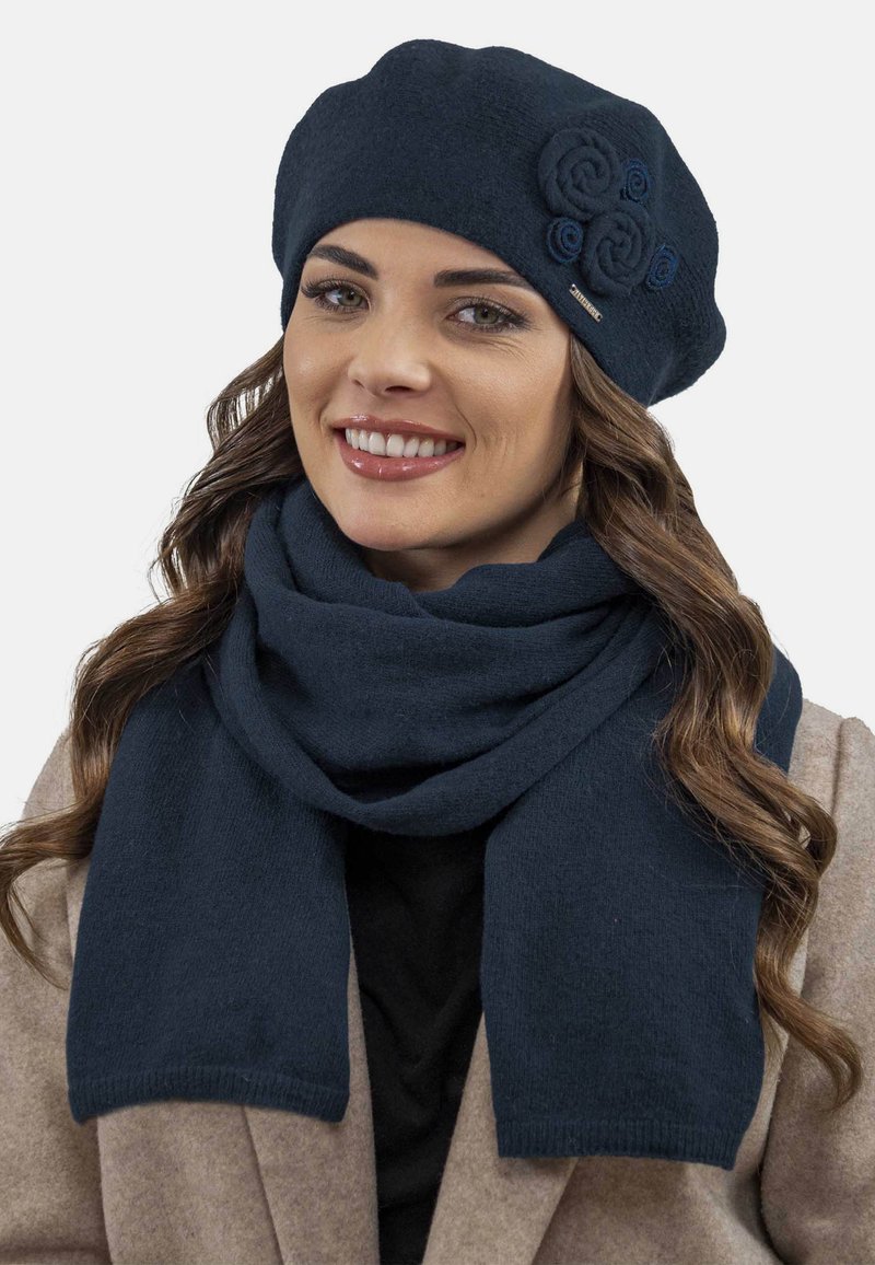 Tengerész kék kötött baret, feltekert virág részletekkel és hozzá illő sállal, puha tapintással és téglalap alakban. Meleg és kényelmes téli kiegészítők.