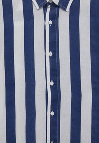 Niebiesko-biała lniana koszula w paski z kołnierzykiem zapinanym na guziki, posiadająca białe guziki oraz teksturowany materiał. Pionowe paski są równo ustawione.