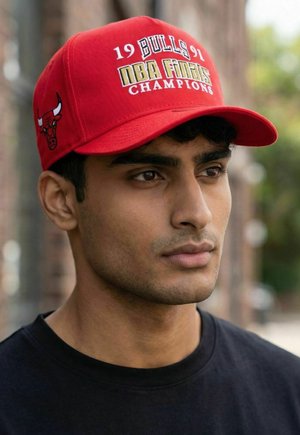 Junger Mann mit roter Chicago Bulls-Kappe mit dem Text NBA Finals Champions 1991, schaut nach seitlich, im Freien mit verschwommenem Hintergrund.