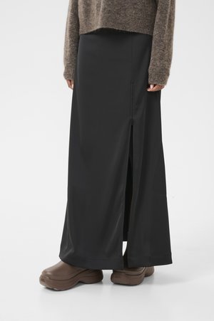 Gonna maxi nera con dettaglio della zip laterale, realizzata in tessuto liscio. Abbinata a un maglione marrone morbido e scarpe marroni.