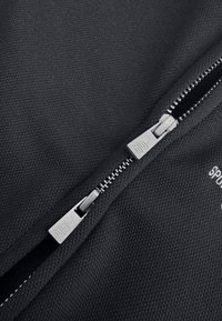 Zwart stof met een gestructureerd oppervlak heeft een zilveren rits en trekkoord, en vertoont verfijnde details en een strakke, nette uitstraling.