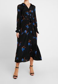 Robe noire à manches longues avec un motif floral bleu et orange. La taille est cintrée par un nœud et elle a un devant à boutons.