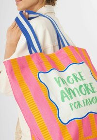 Roze en oranje gestreepte boodschappentas met blauwe handvatten. Bevat een witte patch met groene tekst die zegt "More Amore Por Favor."
