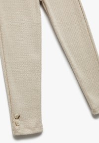 Byxor med beige fiskbensmönster som har en mjuk textur och två små knappar vid fållen.