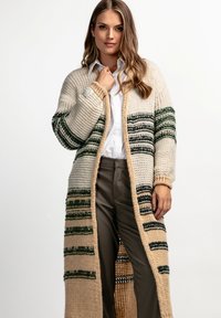 Sweter kardigan w kolorze kremowym z zielonymi i granatowymi paskami, z otwartym przodem, długimi rękawami i wzorem teksturowanym. W połączeniu z białą koszulą i spodniami.