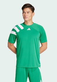 Roheline sportlik shirt lühikeste varrukatega, millel on valged diagonaalsed triibud ja logo. Valmistatud siledast, hingavast kangast.