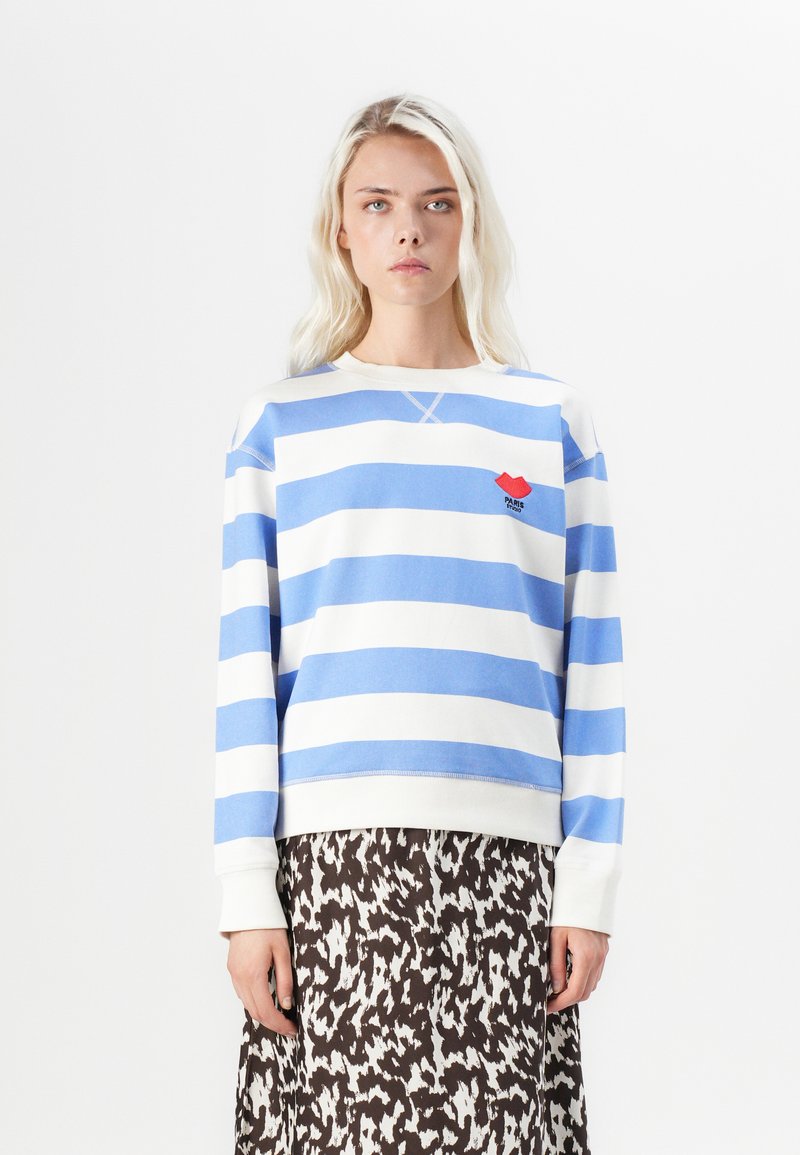 Blue and white striped sweatshirt in a soft fabric, featuring a small red logo on the chest and ribbed cuffs, paired with a patterned skirt.