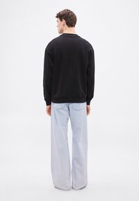 Μαύρο φούτερ με στρογγυλή λαιμόκοψη, άνετη εφαρμογή και μακριά μανίκια, συνδυασμένο με ανοιχτό μπλε τζιν παντελόνι με φαρδιά μπατζάκια και διακριτική υφή τζιν.