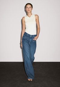 Lys gul ærmeløs top med V-hals, parret med løse, højtaljede blå denimjeans med baglommer og lige ben-design.