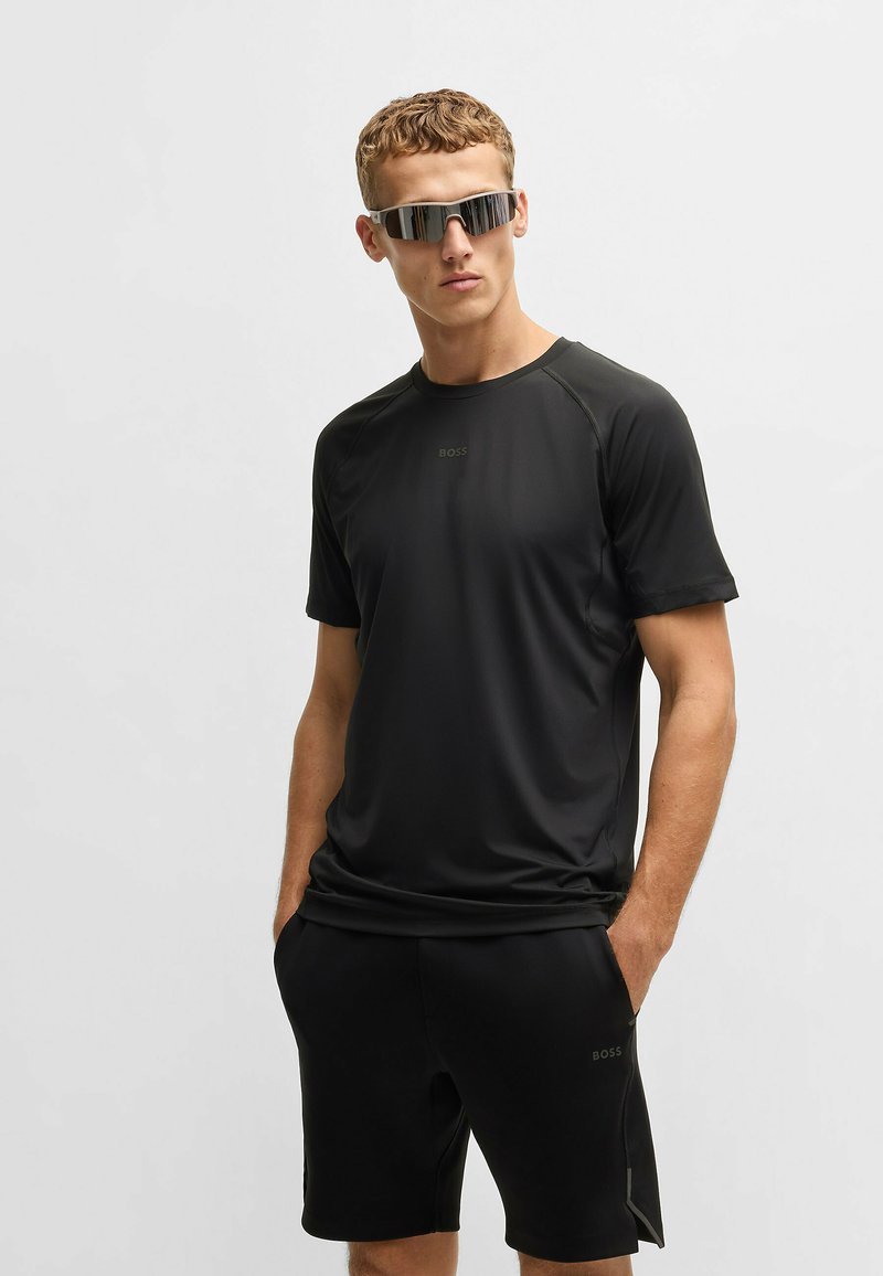 Svart atletisk t-shirt med korta ärmar och rund halsringning, med en subtil logotyp. Kombinationen med svarta shorts, slät textur och minimalistisk design.