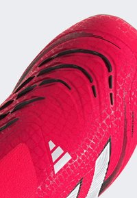 Scarpa sportiva di colore rosa brillante con tomaia texture, dotata di accenti neri, un design a motivi e branding bianco.
