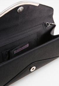 Pochette noire avec extérieur texturé, fermeture pression métallique et poche intérieure avec étiquette logo. Doublure lisse à l'intérieur.