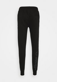 Svarta sweatpants i bomull med elastisk midja, smalnande ben och en subtil logoprint på vänster ben. Mjuk textur.