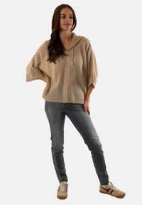 Haut à capuche en tricot beige avec une fermeture éclair à l'avant, coupe ample et manches courtes, associé à un jeans gris et des baskets beige avec des accents bordeaux.