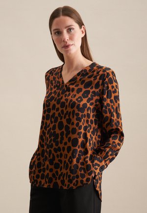 Blusa con stampa leopardata marrone, con scollatura a V e maniche lunghe. Presenta macchie nere e una vestibilità ampia, realizzata in un tessuto morbido.
