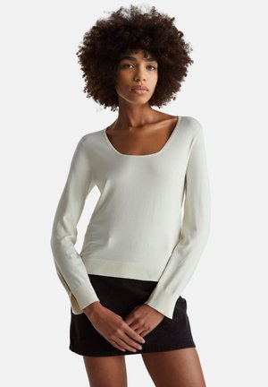 Jasnokremowy sweter z okrągłym dekoltem, długimi rękawami, prążkowanym dołem i bocznymi rozcięciami, w zestawieniu z czarną spódnicą, wykonany z teksturowanej tkaniny, dopasowany fason.