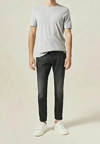 Maglietta grigia a maniche corte abbinata a jeans in denim scuro e sneaker bianche, caratterizzata da un design semplice con una texture liscia e una vestibilità comoda.