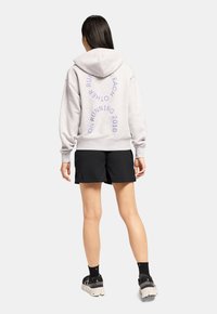 Grauer Hoodie mit einer Kordelzug, der auf der Rückseite blauen Text zeigt. Schwarze Shorts und schwarze Sneakers mit einer hellen Sohle runden das Outfit ab.