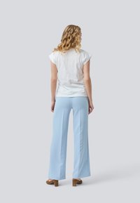 Haut blanc à manches courtes associé à un pantalon large bleu clair, texture lisse, avec une coupe décontractée et un design simple. Des talons marron complètent la tenue.