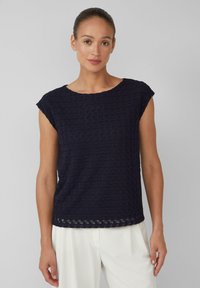 Haut bleu marine à manches courtes avec un motif géométrique texturé, un col rond et une coupe légèrement ample, associé à un pantalon de couleur claire.