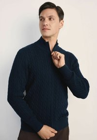 Granatowy sweter zapinany na zamek, pleciony w wzór warkocz, z ryżowymi mankietami i dolnym brzegiem, z wysokim kołnierzem i gładką fakturą.