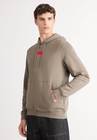 Felpa con cappuccio in cotone misto verde oliva, presenta una tasca frontale a marsupio, polsini a coste e un'etichetta rettangolare rossa con la scritta "HUGO."