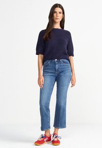 Navy wool-blend short-sleeve sweater, medium wash high-waisted jeans, and red sneakers with blue and white laces, standing against a light background.