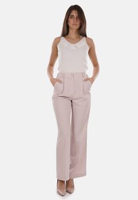 Pantaloni a vita alta rosa chiaro con pieghe frontali e tasche, abbinati a un top bianco senza maniche con dettagli floreali ricamati.