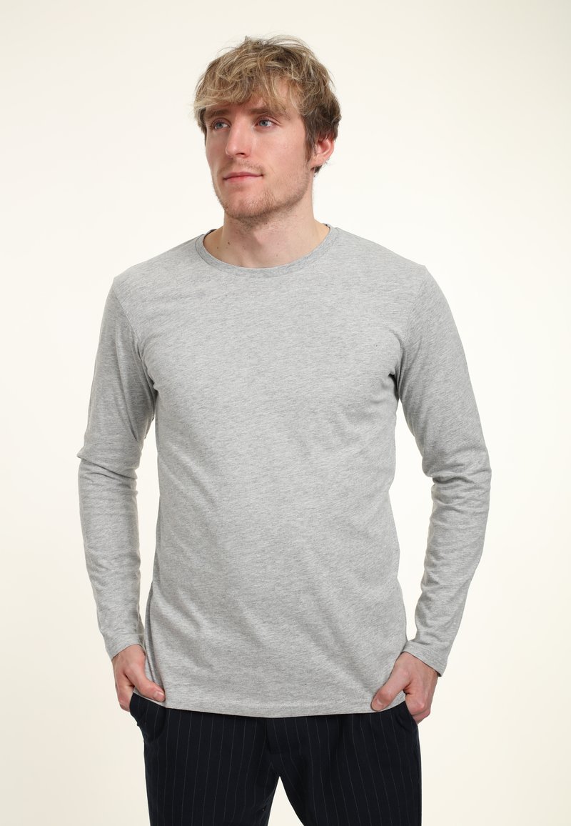 Šedá halenka s dlouhým rukávem a kulatým výstřihem, vyrobená z měkké tkaniny. Obsahuje jednoduchý design, těsný střih a hladkou texturu. Kombinována s tmavými pruhovanými kalhotami.