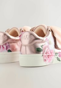 Des baskets en rose doré métallique ornées de motifs floraux, avec une semelle en caoutchouc blanche et des nœuds en satin à l'avant, offrant un aspect texturé et féminin.